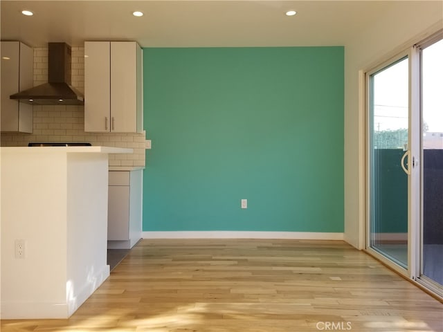 kitchen featuring wall chimney exhaust hood, white cabinets, decorative backsplash, and light hardwood / wood-style flooring