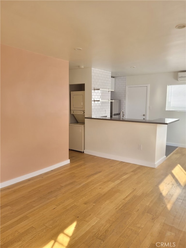 unfurnished living room with sink, light wood-type flooring, stacked washer / drying machine, and a wall unit AC