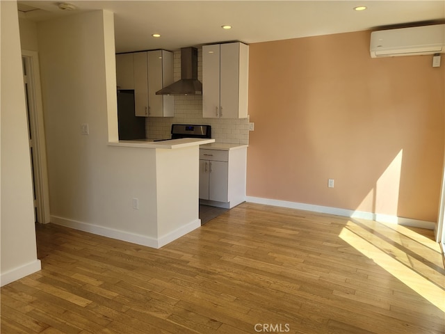 kitchen with wall chimney exhaust hood, light hardwood / wood-style flooring, refrigerator, a wall mounted air conditioner, and decorative backsplash