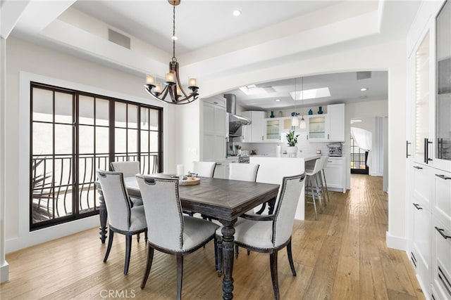 dining space with light wood-type flooring, a tray ceiling, and a notable chandelier