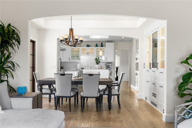 1165 Noria St, Laguna Beach, CA 92651 - dining area featuring a chandelier, light wood-type flooring, arched walkways, and a raised ceiling
