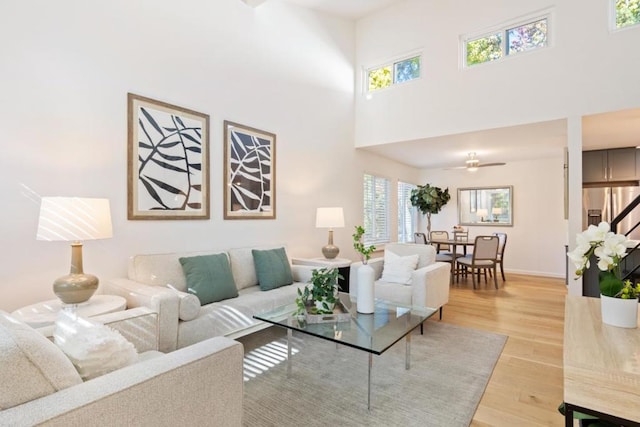 living room with ceiling fan, a towering ceiling, and light wood-type flooring