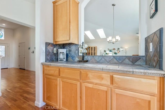 kitchen featuring light brown cabinets, hanging light fixtures, light hardwood / wood-style flooring, a skylight, and tasteful backsplash