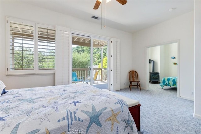 carpeted bedroom with access to outside, a wood stove, and ceiling fan