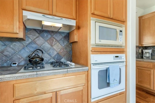 kitchen with hardwood / wood-style flooring, white appliances, and tasteful backsplash