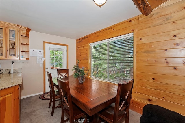 dining space with vaulted ceiling with beams, wood walls, a healthy amount of sunlight, and dark colored carpet