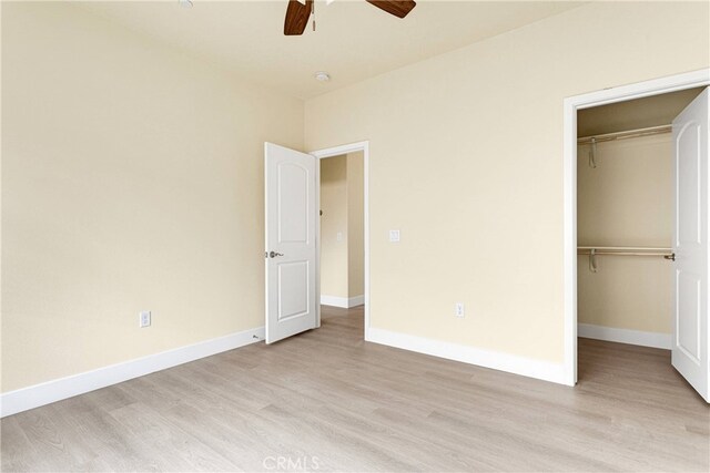 unfurnished bedroom featuring a closet, light wood-type flooring, ceiling fan, and a walk in closet