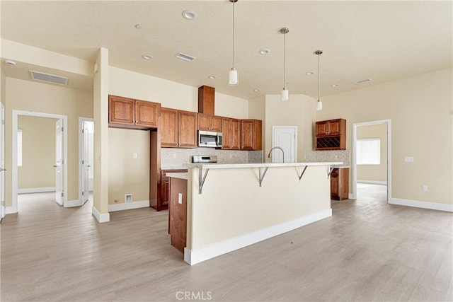 kitchen featuring light hardwood / wood-style flooring, a kitchen breakfast bar, hanging light fixtures, and a kitchen island with sink