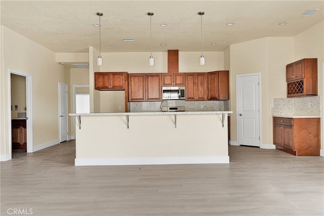 kitchen featuring pendant lighting, a center island with sink, backsplash, and a breakfast bar