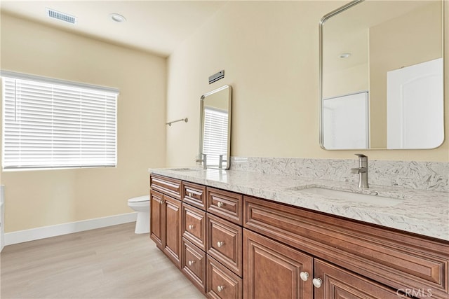 bathroom with a healthy amount of sunlight, wood-type flooring, vanity, and toilet