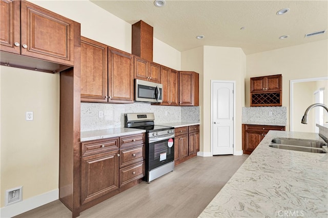 kitchen with appliances with stainless steel finishes, decorative backsplash, light wood-type flooring, and sink