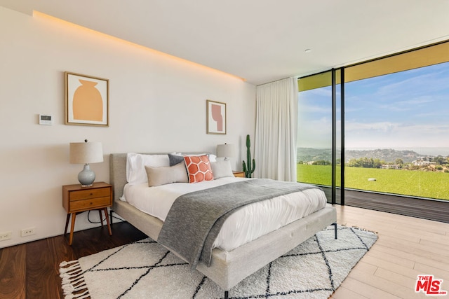 bedroom featuring access to exterior, floor to ceiling windows, a mountain view, and hardwood / wood-style flooring