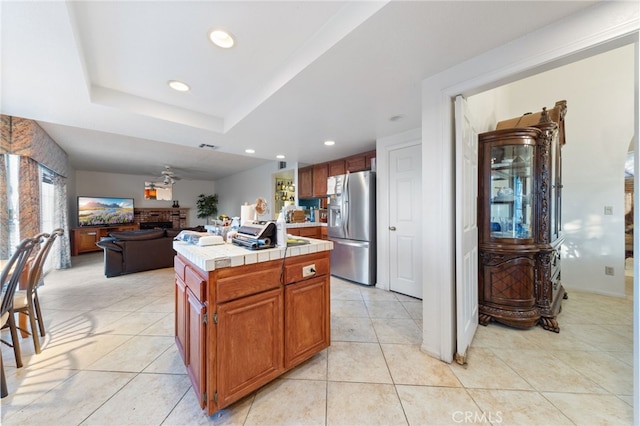 kitchen with ceiling fan, a center island, a brick fireplace, stainless steel refrigerator with ice dispenser, and tile countertops