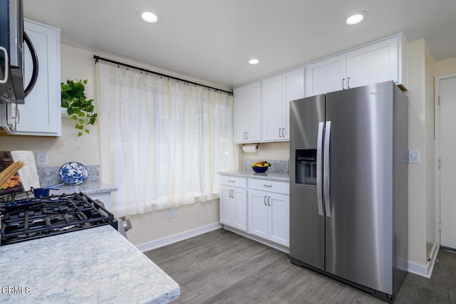 kitchen with appliances with stainless steel finishes, light hardwood / wood-style flooring, white cabinetry, and light stone counters