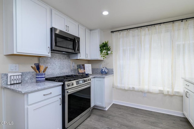 kitchen featuring light stone countertops, white cabinetry, light hardwood / wood-style floors, and appliances with stainless steel finishes