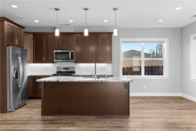 kitchen with appliances with stainless steel finishes, light hardwood / wood-style floors, light stone countertops, pendant lighting, and sink