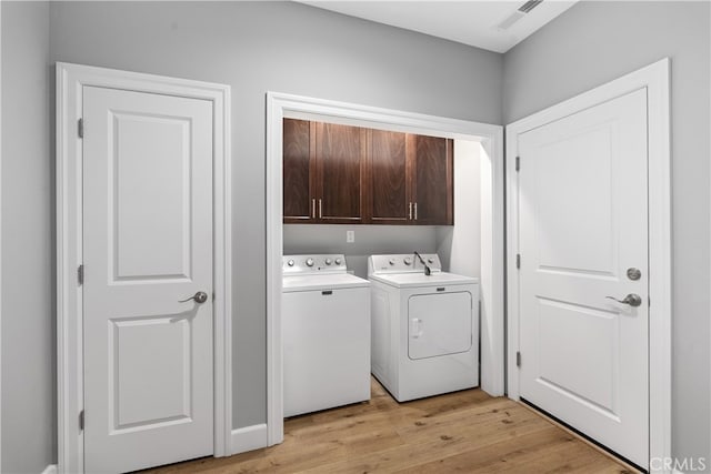 clothes washing area with light hardwood / wood-style floors, independent washer and dryer, and cabinets