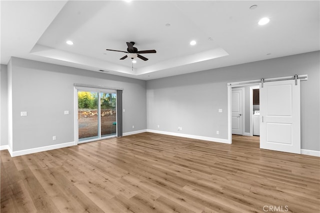 empty room featuring light hardwood / wood-style flooring, ceiling fan, a raised ceiling, and a barn door