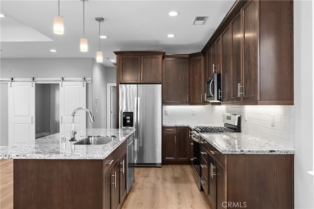 kitchen featuring sink, a center island with sink, appliances with stainless steel finishes, a barn door, and light hardwood / wood-style floors