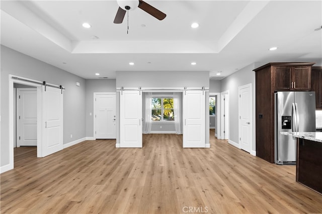 interior space featuring a barn door, light wood-type flooring, ceiling fan, and a tray ceiling