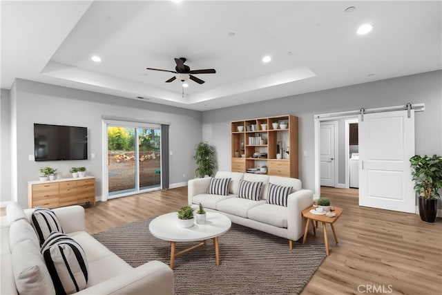 living room featuring washer / dryer, hardwood / wood-style flooring, a barn door, a raised ceiling, and ceiling fan