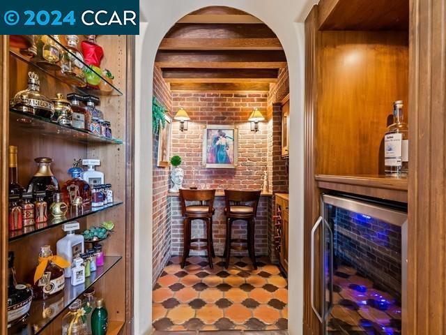 bar with beamed ceiling, beverage cooler, and brick wall