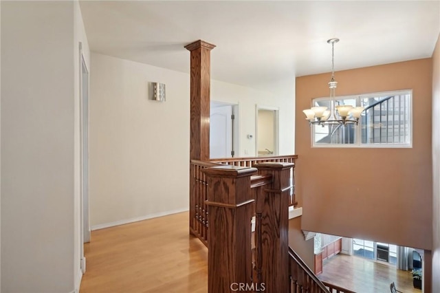 hall featuring a chandelier, light hardwood / wood-style floors, and decorative columns