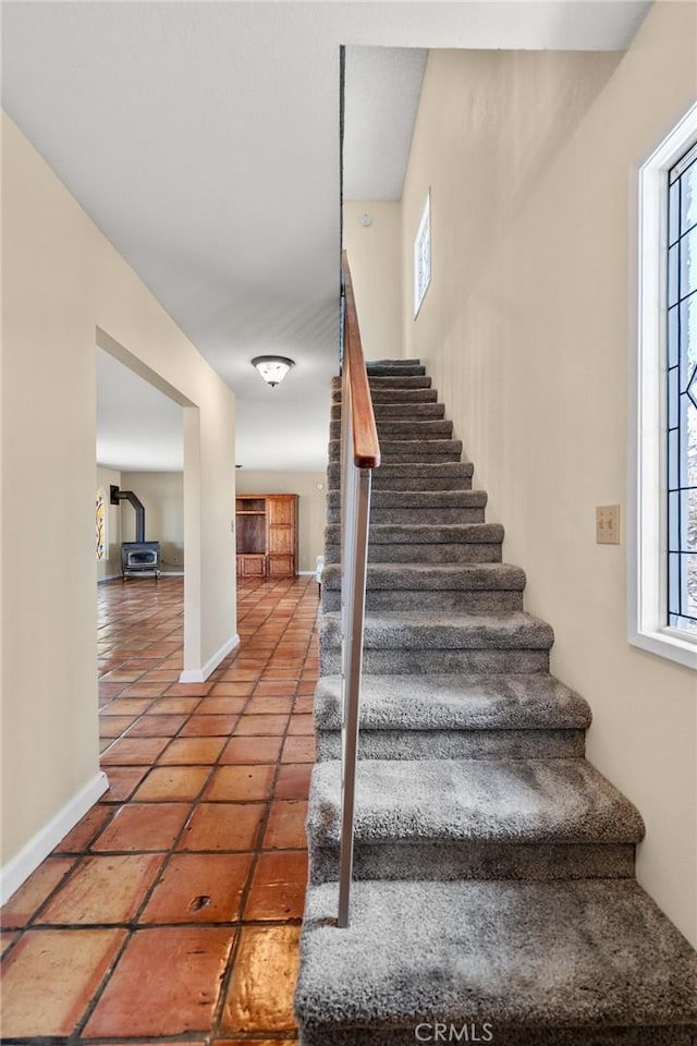 stairway featuring tile patterned floors, a wood stove, and a healthy amount of sunlight