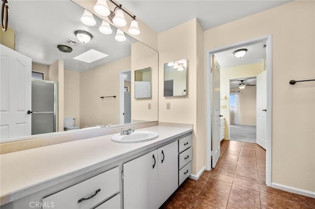 bathroom featuring a skylight, vanity, ceiling fan, a shower with door, and toilet