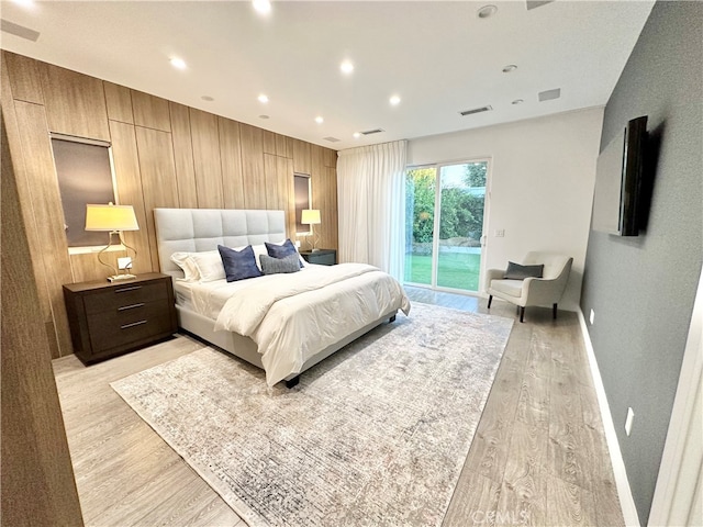 bedroom with light wood-type flooring, wood walls, and access to outside