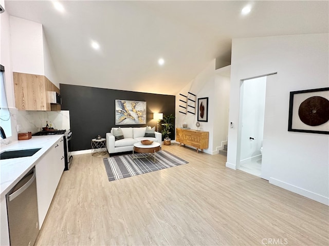 kitchen featuring vaulted ceiling, dishwasher, light hardwood / wood-style flooring, sink, and light stone counters