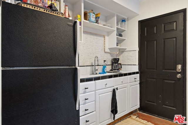 kitchen featuring tasteful backsplash, white cabinets, light hardwood / wood-style flooring, tile countertops, and black refrigerator