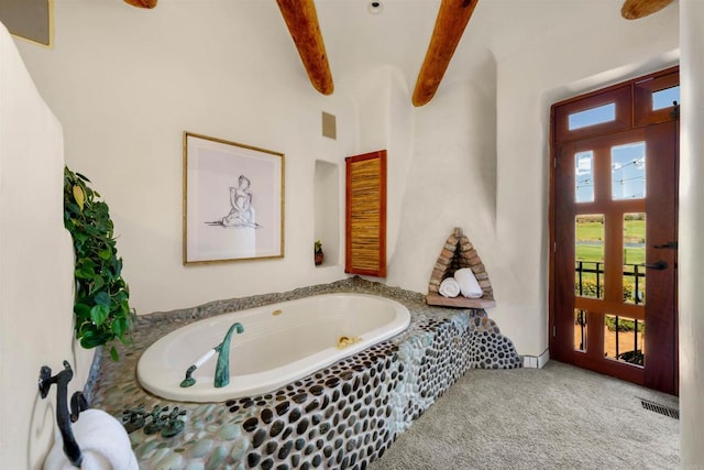 bathroom featuring a relaxing tiled tub and beamed ceiling