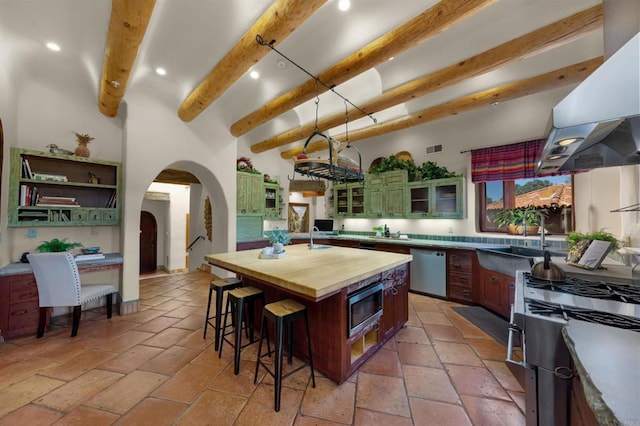 kitchen featuring beam ceiling, sink, appliances with stainless steel finishes, an island with sink, and wood counters