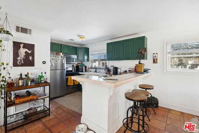 kitchen with appliances with stainless steel finishes, kitchen peninsula, tile countertops, a kitchen bar, and green cabinets