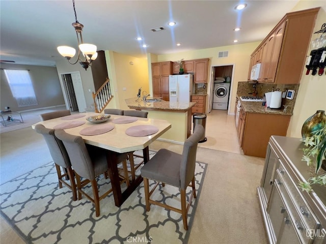 dining space featuring washer / dryer, light colored carpet, and a notable chandelier