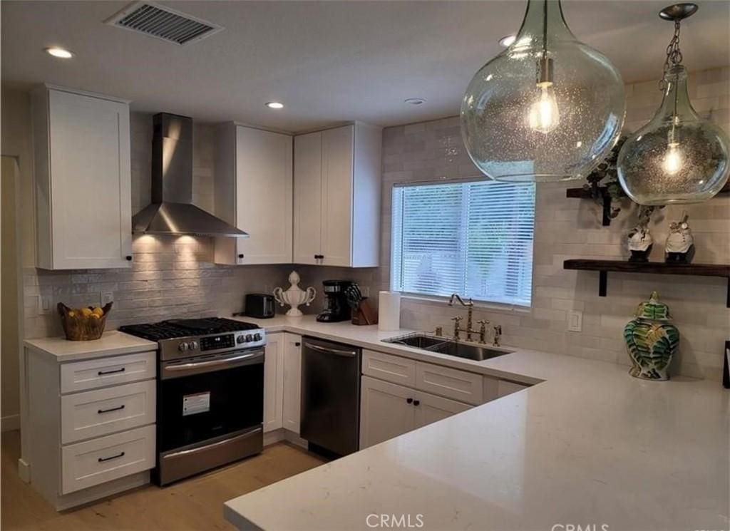kitchen with visible vents, dishwashing machine, wall chimney exhaust hood, a sink, and gas stove