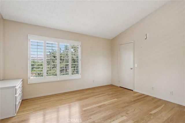 spare room with light hardwood / wood-style floors and lofted ceiling