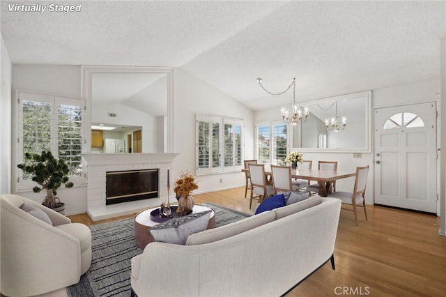 living room with a brick fireplace, vaulted ceiling, a healthy amount of sunlight, and hardwood / wood-style floors