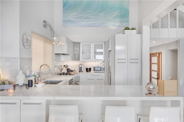 kitchen with appliances with stainless steel finishes, backsplash, white cabinetry, and light stone counters