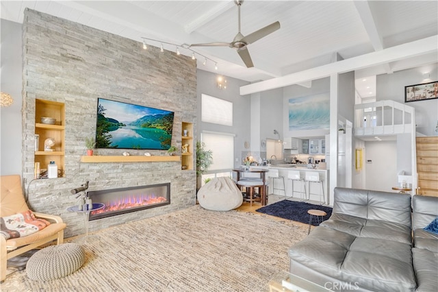 living room featuring a stone fireplace, a high ceiling, beam ceiling, and ceiling fan