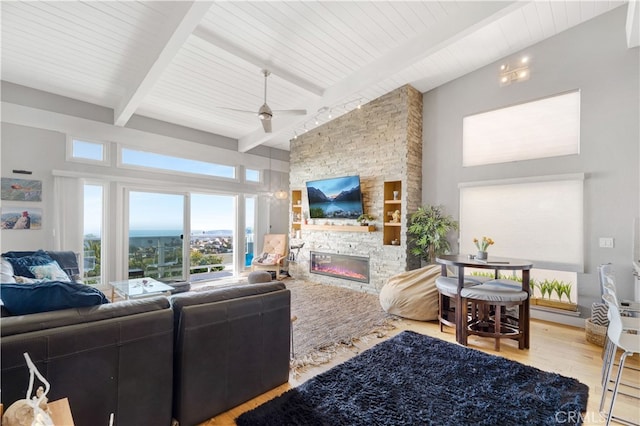 living room featuring ceiling fan, beamed ceiling, a stone fireplace, high vaulted ceiling, and light wood-type flooring