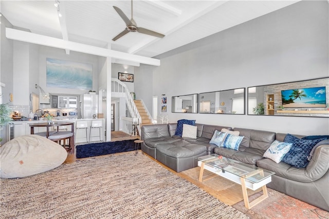 living room featuring ceiling fan, beamed ceiling, a high ceiling, and hardwood / wood-style flooring