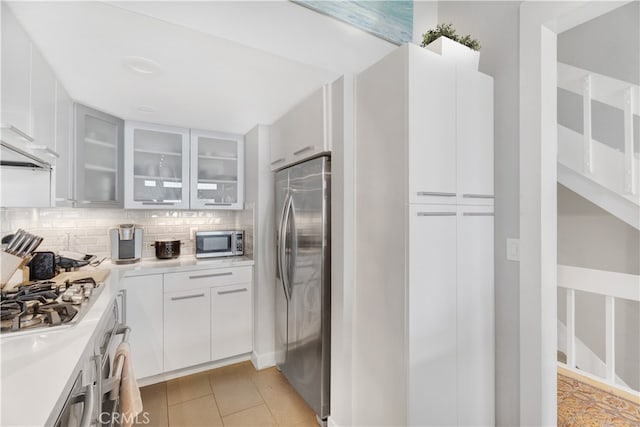 kitchen featuring appliances with stainless steel finishes, light tile patterned floors, tasteful backsplash, and white cabinetry