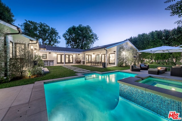 pool at dusk featuring a yard, an outdoor living space, an in ground hot tub, and a patio area