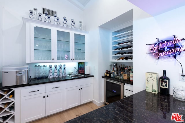 bar featuring wine cooler, light hardwood / wood-style floors, sink, white cabinets, and dark stone countertops