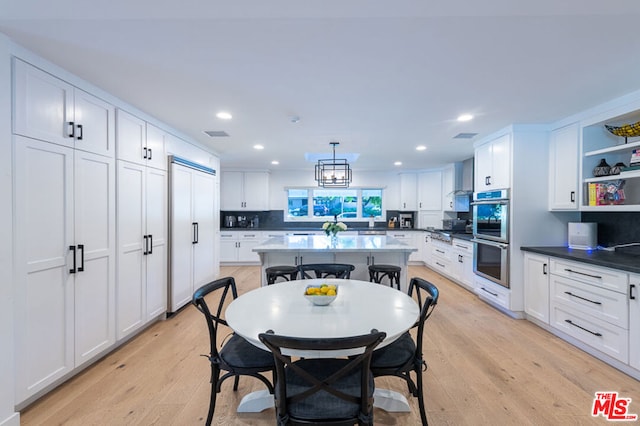 kitchen with hanging light fixtures, light hardwood / wood-style floors, stainless steel appliances, and white cabinets