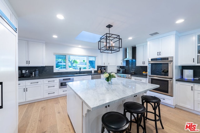 kitchen featuring wall chimney exhaust hood, light hardwood / wood-style floors, white cabinetry, and a center island