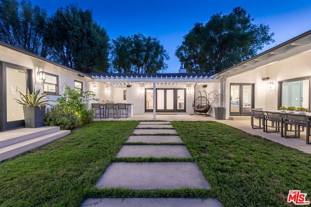 back house at dusk featuring a patio, a yard, an outdoor bar, and french doors