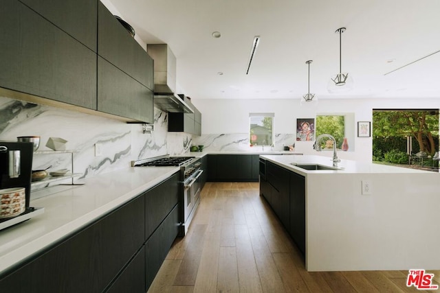 kitchen featuring pendant lighting, light wood-type flooring, sink, stainless steel stove, and decorative backsplash